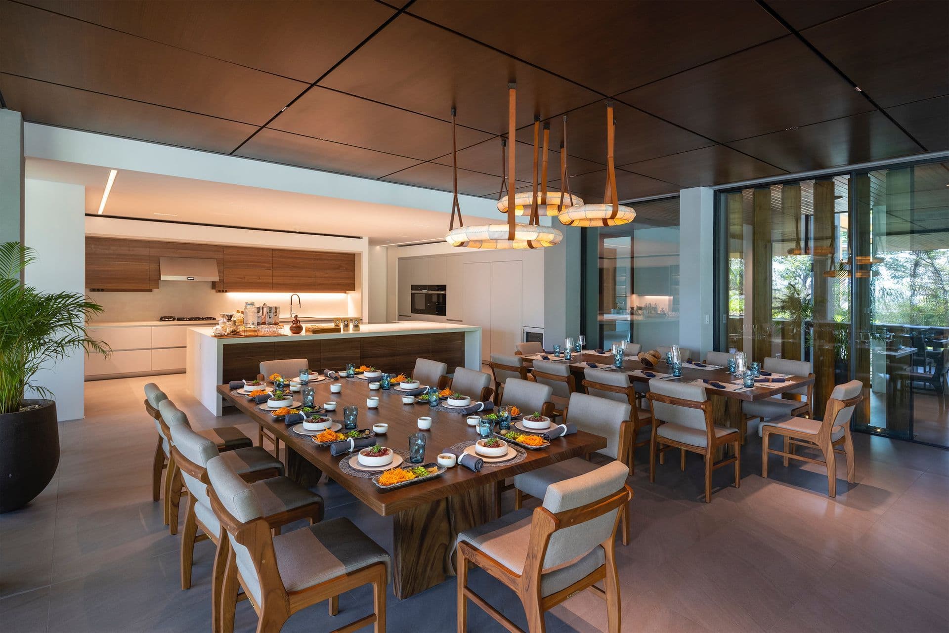 A generous dining table beneath a warm timber ceiling, beside an open kitchen.