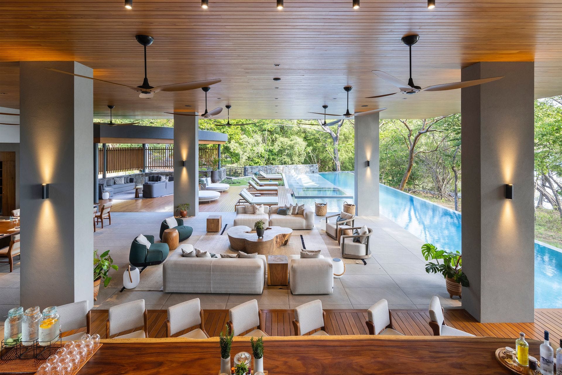 Daylight reaches an open lounge, with timber ceilings, quiet seating and a long pool beyond.
